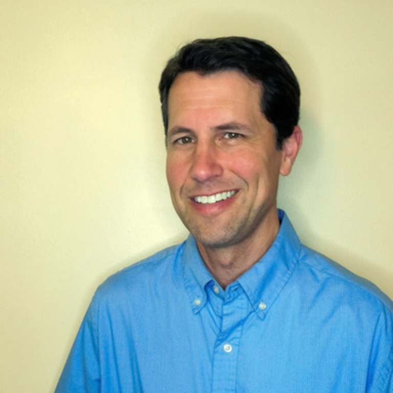 A photograph of a man in a blue shirt in front of a yellow background